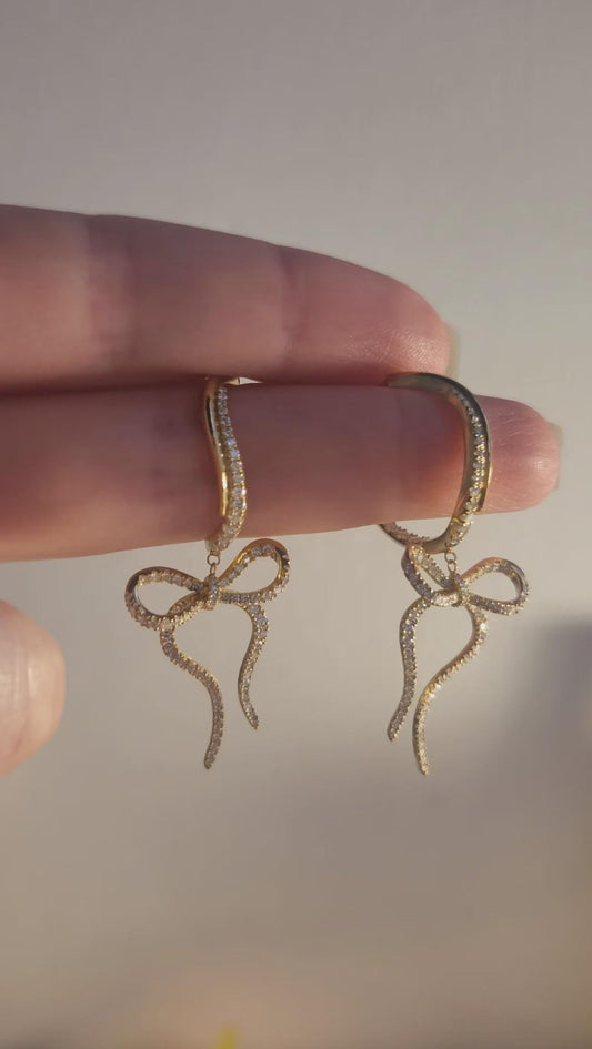 Pair of Wavy Bow Diamond Hoops in 18K yellow gold held in hand, handmade jewelry in the age of AI for Los Angeles creatives